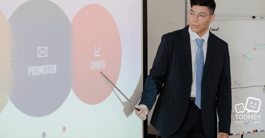 A presenter pointing to visuals and describing them. Toomey Business English.