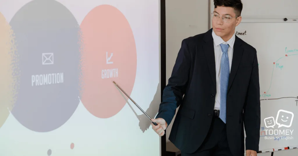 A presenter pointing to visuals and describing them. Toomey Business English.