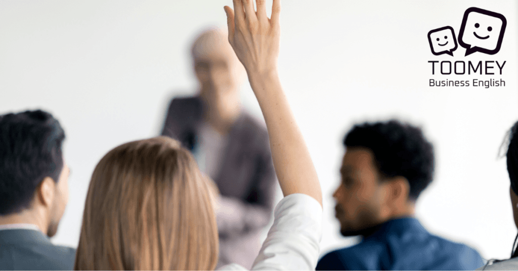 Audience member raises a hand to ask the presenter a question. Toomey Business English.