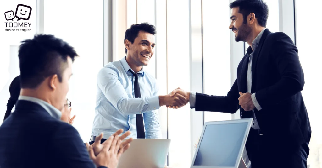 Two men shaking hands in the office. Toomey Business English.